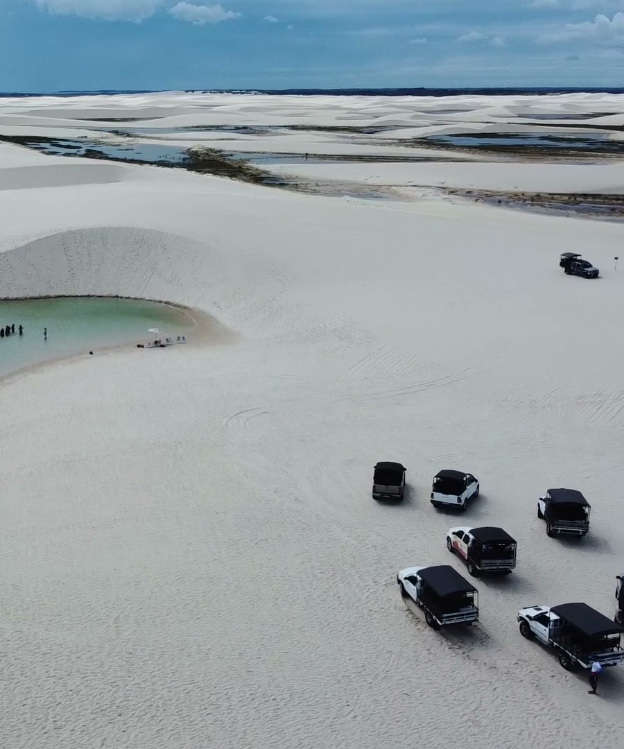 Veículos 4x4 estacionados ao lado de uma lagoa nos Lençóis Maranhenses